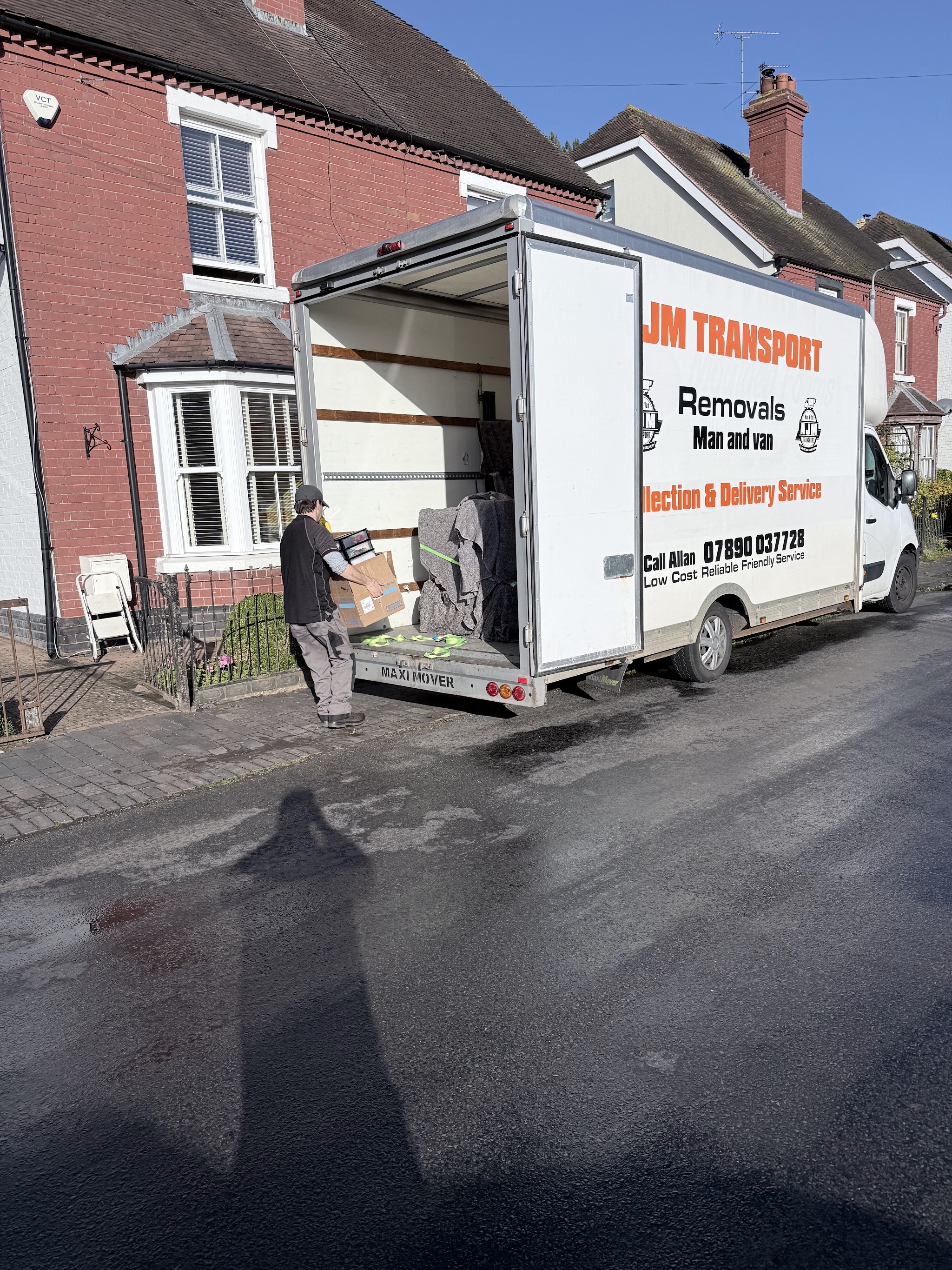 An AJM Transport team member carrying a box up the tail lift into the van outside a terraced house