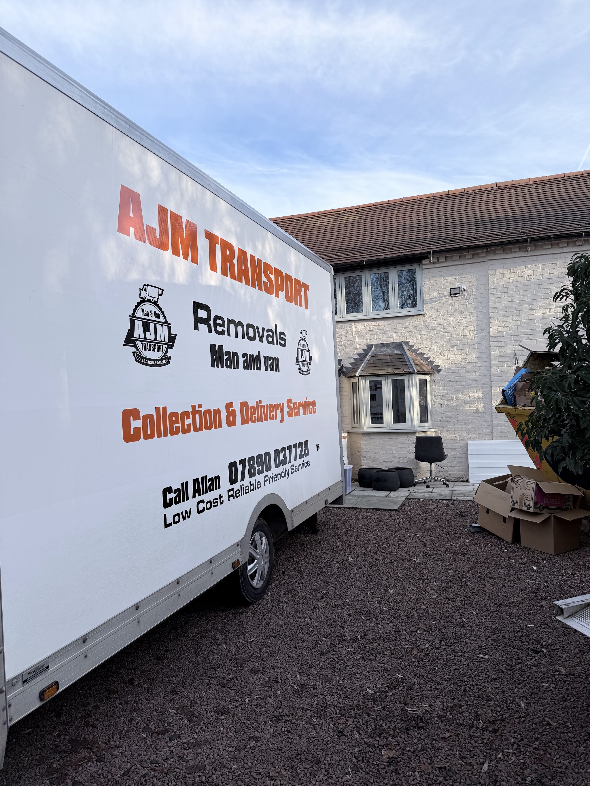 The AJM Transport van with its orange livery parked beside a white-painted cottage during a move